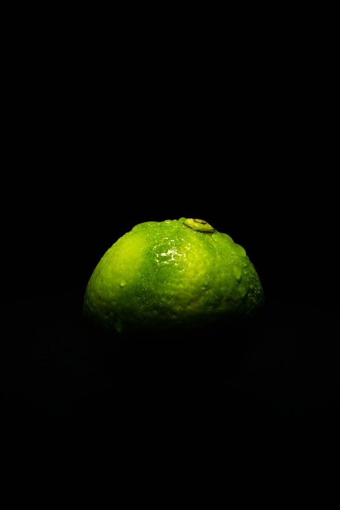Grüne Limette im Halbschatten vor schwarzem Hintergrund